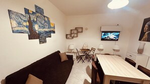 Un salon avec un canapé marron foncé, une table à manger en bois avec des chaises, et un téléviseur à écran plat fixé au mur.