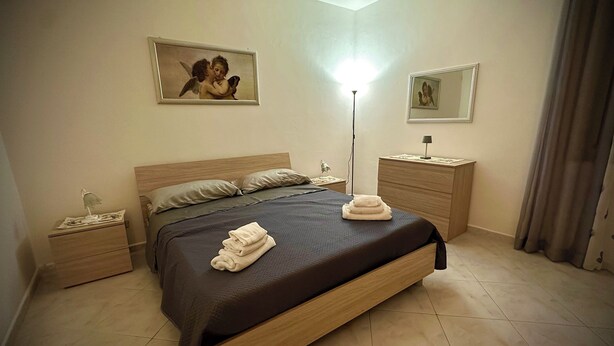 Une chambre d’hôtel avec un lit, des tables de chevet, une lampe, un miroir et des œuvres d’art accrochées aux murs.