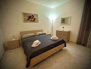 Una habitación de hotel con cama, mesitas de noche, lámpara, espejo y obras de arte en las paredes.