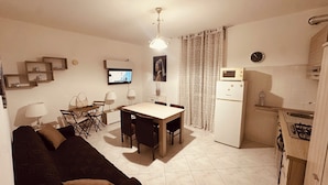 Un espace de vie compact comprenant un canapé, une table à manger, des chaises, un téléviseur, un four à micro-ondes et un coin cuisine.