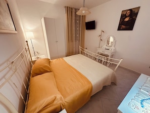A bedroom with a bed, a wardrobe, a desk with a mirror, and a painting on the wall.