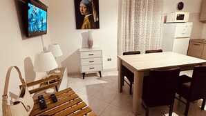 Un salon moderne avec un téléviseur à écran plat, un tableau, une table à manger avec des chaises, un canapé, une lampe et une télécommande posée sur le sol.