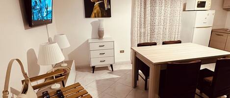 Una sala de estar moderna con una televisión de pantalla plana, un cuadro, una mesa de comedor con sillas, un sofá, una lámpara y un control remoto en el suelo.