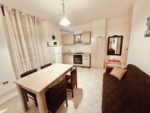 Un espacio habitable compacto con una mesa de comedor, sillas, un sofá, kitchenette y un espejo.
