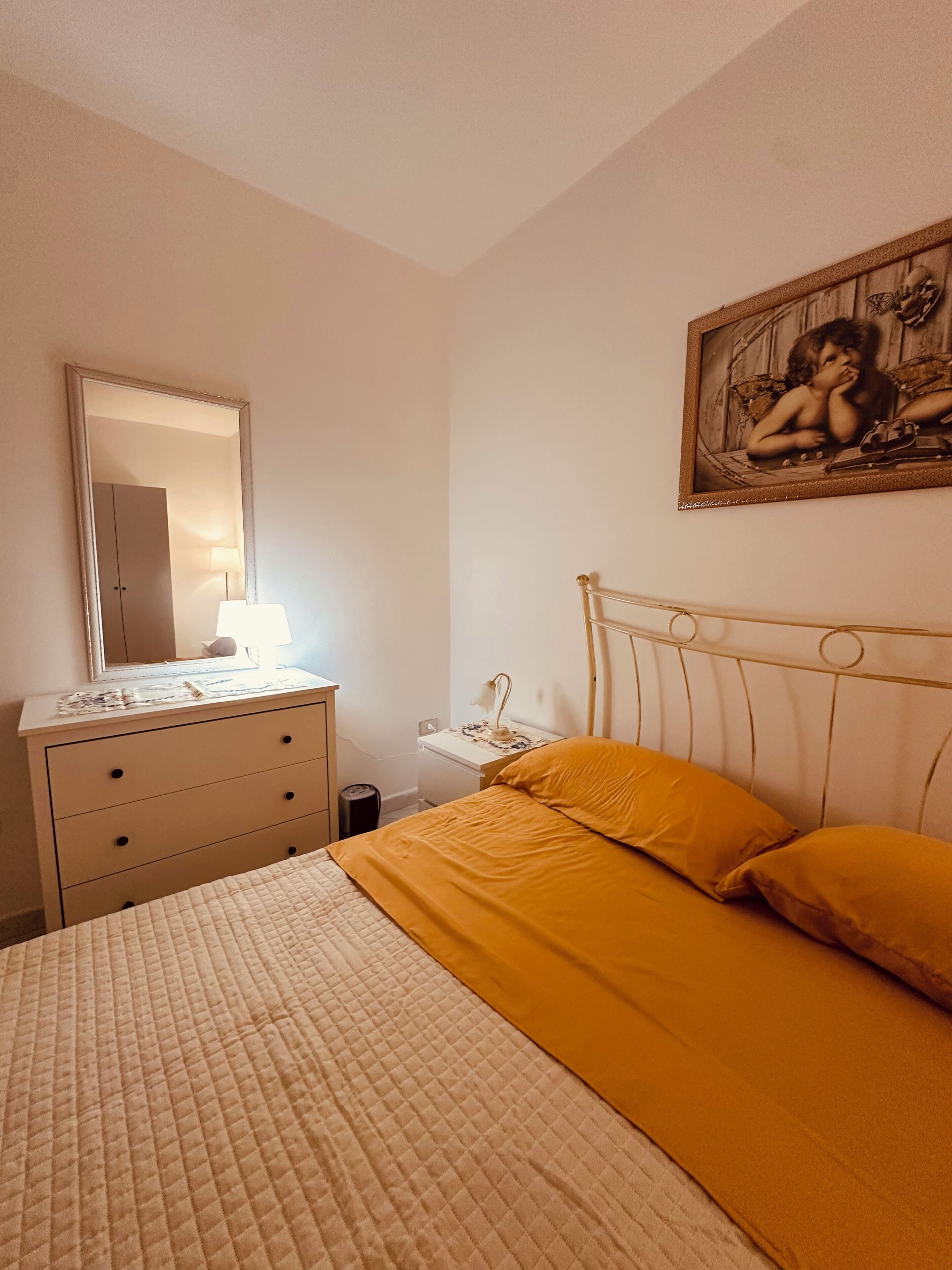 Een slaapkamer met een bed, een kaptafel, een nachtkastje, een lamp en een schilderij aan de muur.