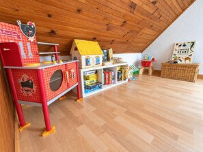 A children's play area with a red play kitchen, a yellow playhouse, and a bookshelf filled with toys and books.