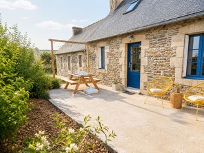 A stone building with a blue door, a wooden table with chairs, and a garden area.