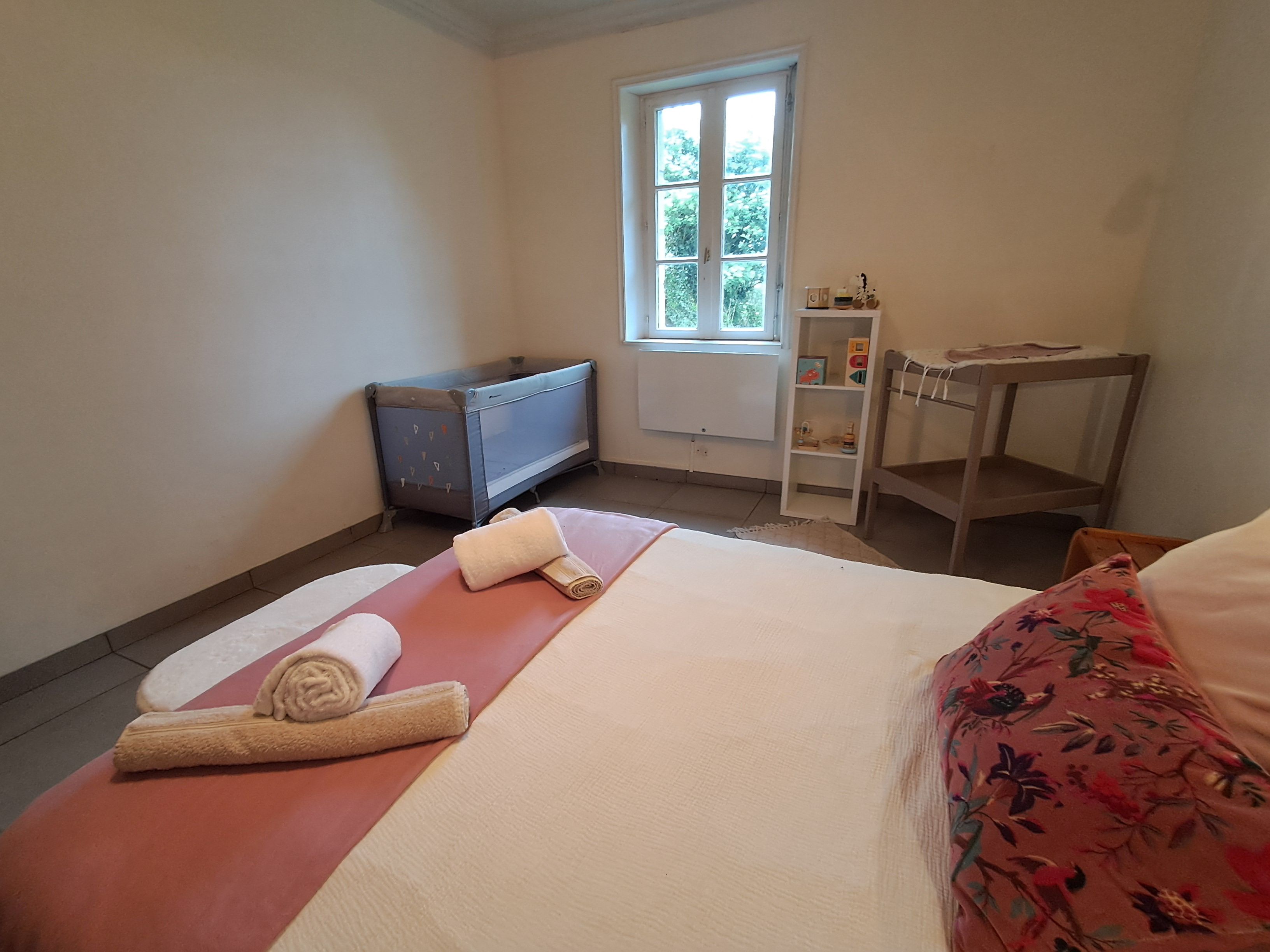 A bedroom with a bed, a small table, a radiator, and a window.