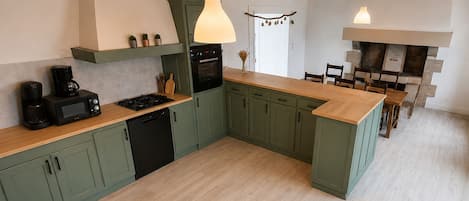 A modern kitchen with green cabinets, a wooden countertop, a built-in oven, and pendant lighting.