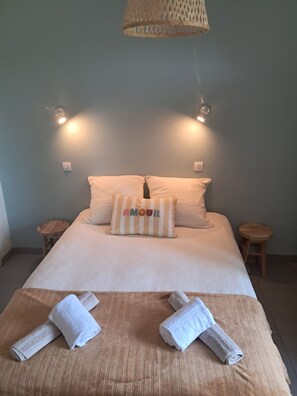 Un lit bien fait, avec des oreillers, un coussin rayé orné du mot «AMOUR», et deux serviettes enroulées posées sur une tête de lit en bois.
