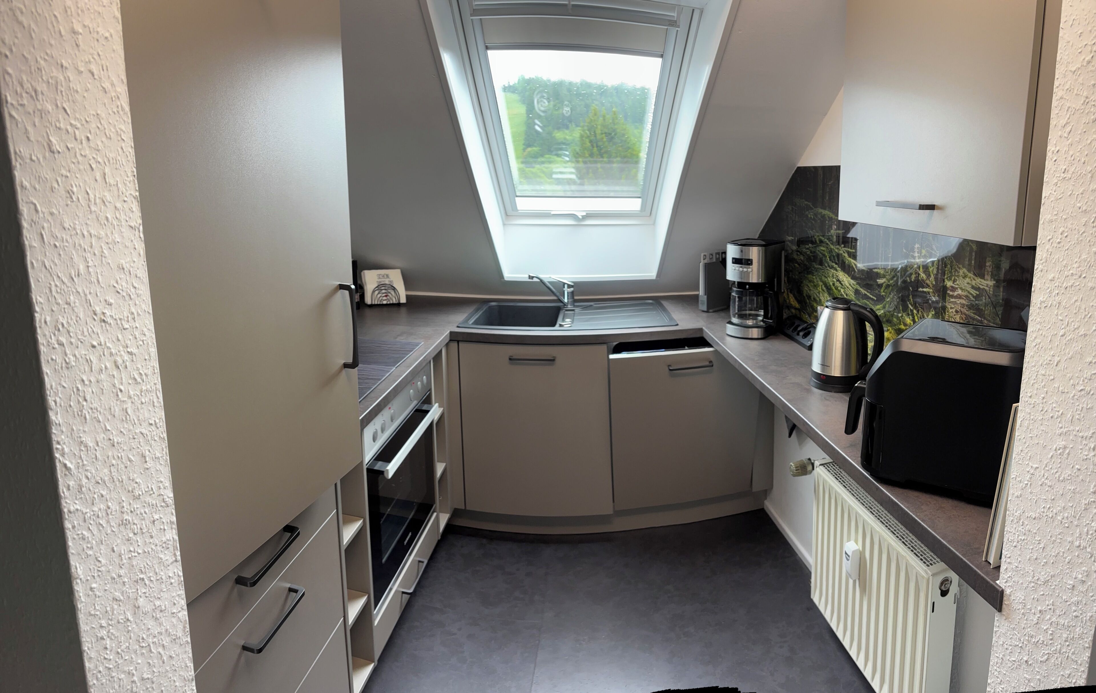 Eine kleine Küche mit integriertem Backofen, Spüle und Kaffeemaschine.