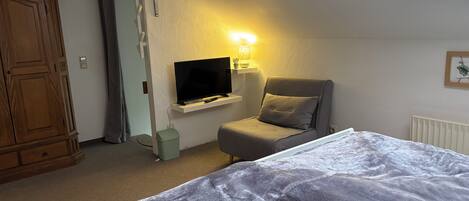 A bedroom with a bed, a television, a chair, and a small window.