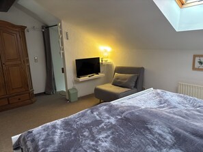 A bedroom with a bed, a television, a chair, and a small window.