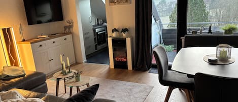 A modern living room with a sofa, a dining table, and a kitchen area visible through an open door.