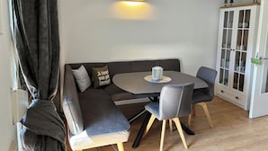 A modern dining area with a dark gray sectional sofa, two gray chairs, a round table, and a wall-mounted light fixture.