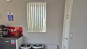A compact living space with a kitchenette, a sofa, and two trash bins. - Room-cozy Guest Room With Modern Ameniti (Tipton)