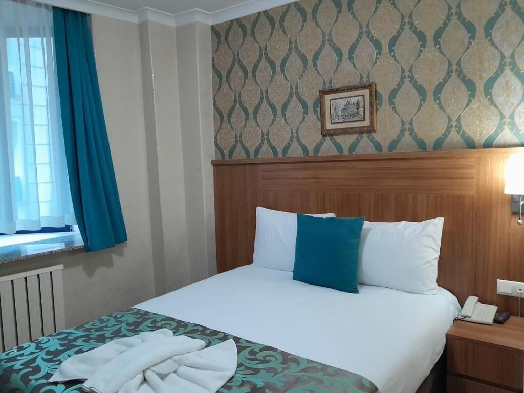 Une chambre d’hôtel avec un lit, une table de chevet, un téléphone et une fenêtre avec des rideaux.