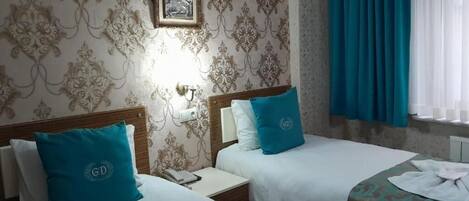 Quarto de hotel com duas camas, mesa de cabeceira, luminária na parede e janela com cortinas.