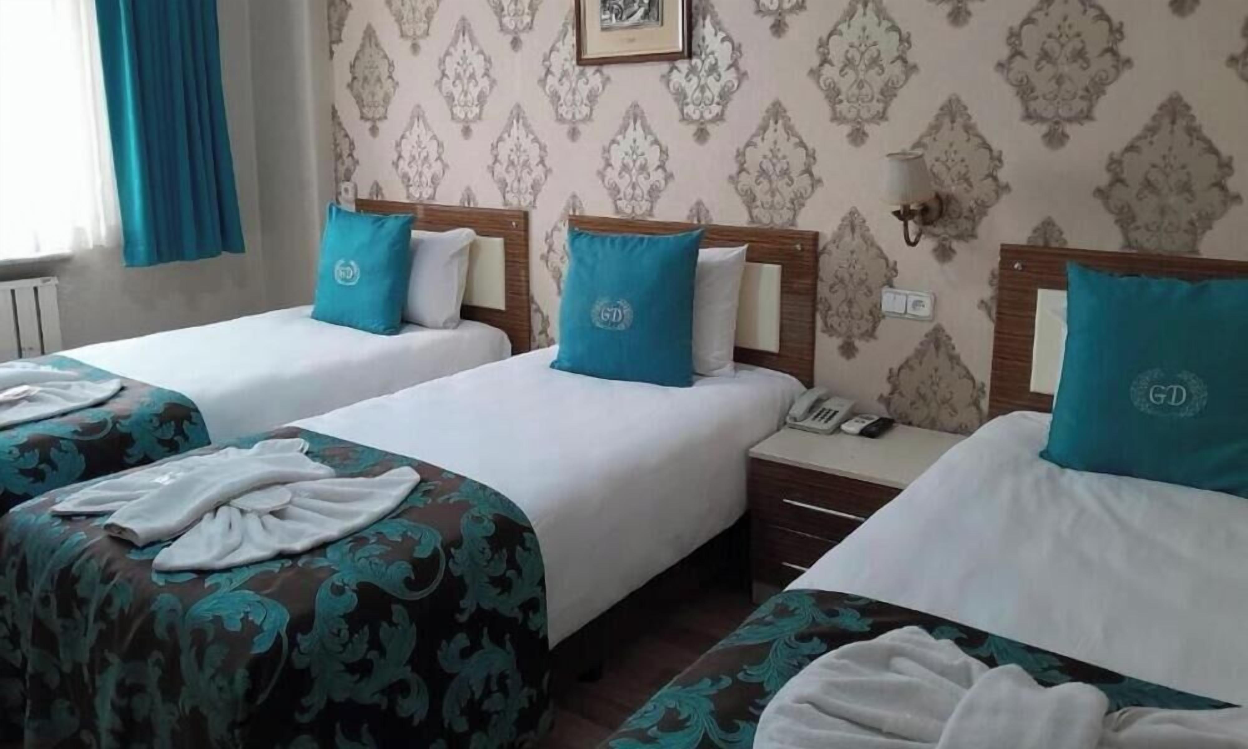 Une chambre d’hôtel avec trois lits, chacun doté d’une tête de lit et d’un oreiller. Il y a une table de chevet avec une lampe et un téléphone dessus.