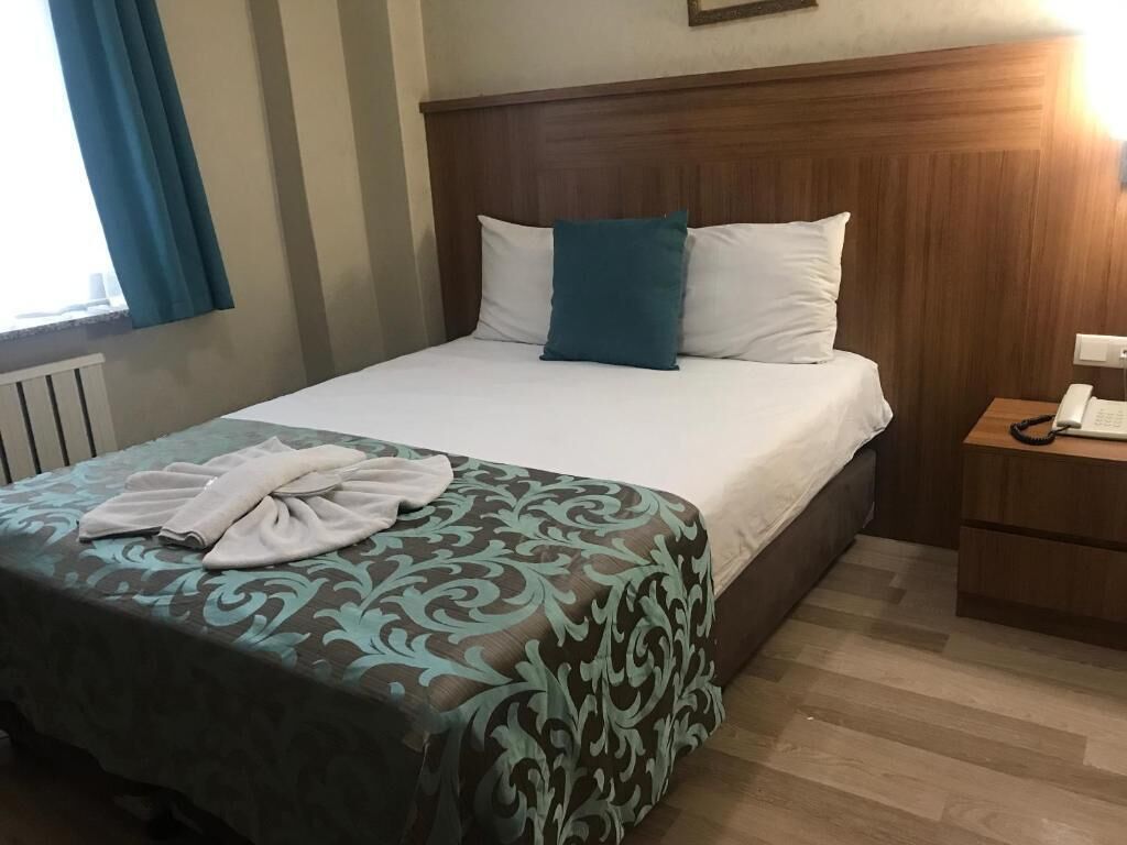 A hotel room with a bed, a bedside table with a phone, and a window with curtains.