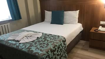 A hotel room with a bed, a bedside table with a phone, and a window with curtains.