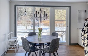 Ein Essbereich mit einem runden Tisch, vier Stühlen, einer Chandelierleuchtre und Blick auf eine verschneite Landschaft durch große Fenster.