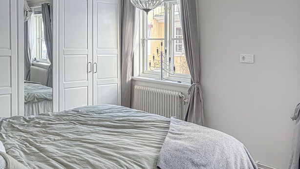 Une chambre à coucher avec un lit, un radiateur et une fenêtre avec des rideaux.