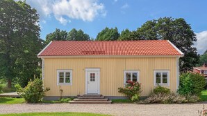 Une maison à deux étages, avec un toit recouvert de tuiles rouges, une porte d’entrée et un petit porche.