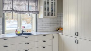 Une cuisine avec des meubles blancs, une fenêtre donnant sur un paysage enneigé et un panier de fruits posé sur le comptoir.