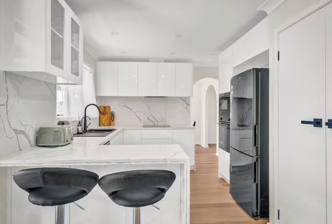 Una cocina moderna con armarios blancos, salpicadero de mármol y refrigerador negro.