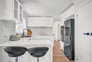 A modern kitchen with white cabinetry, a marble backsplash, and a black refrigerator.