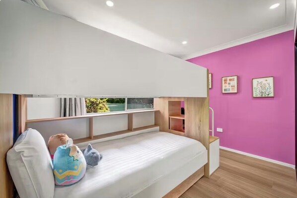 A bunk bed with a window, a pink wall, and a small shelf.