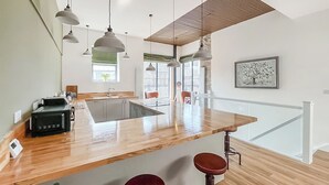 Eine moderne Küche mit Holzarbeitsplatte, Barhocker, Pendelleuchten und Blick ins Freie.