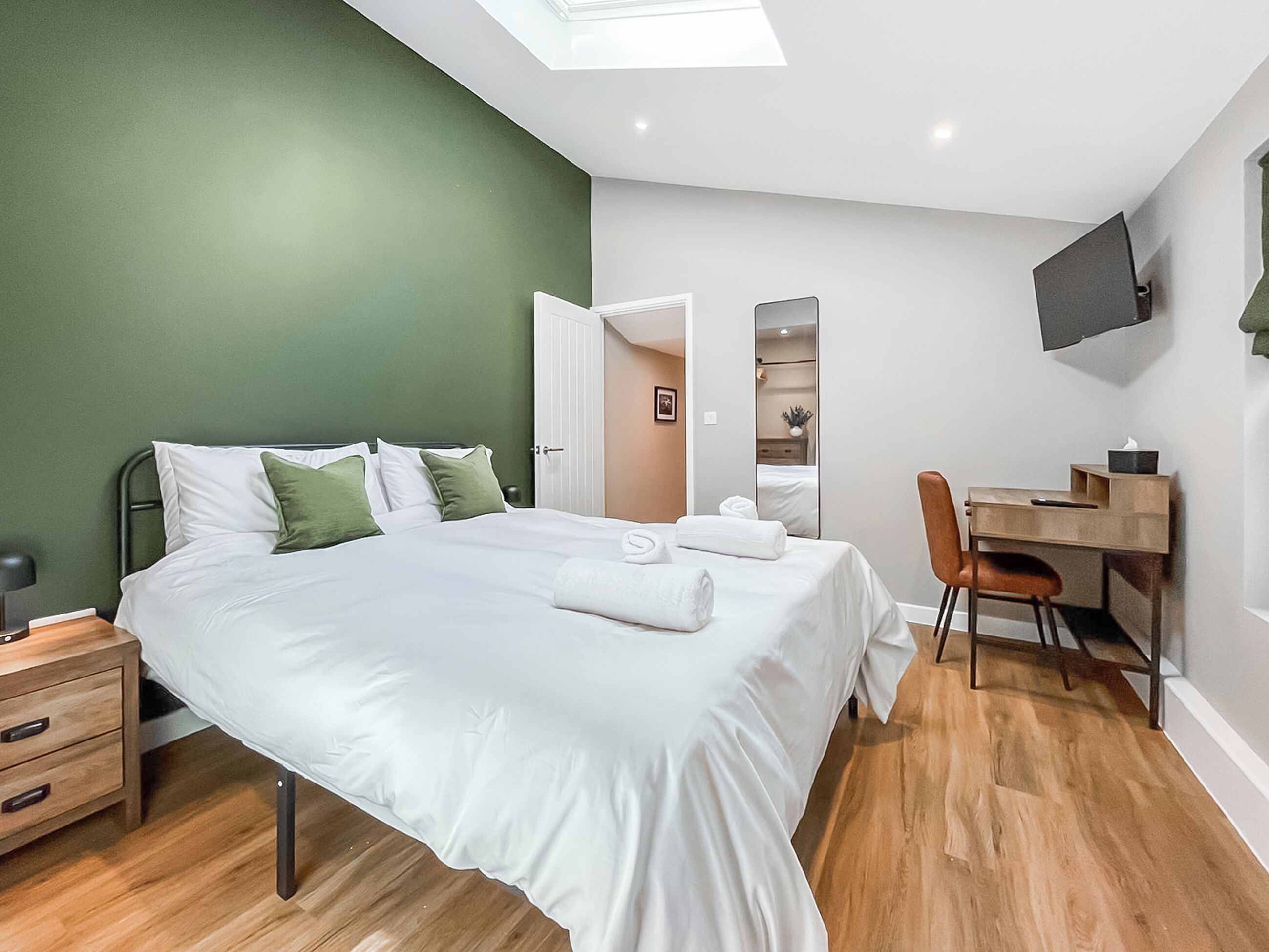 A bedroom with a bed, a desk, a chair, a TV, and a door leading to another room.