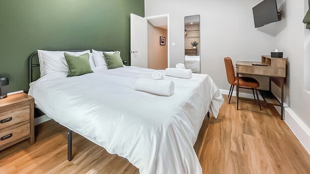 Ein Schlafzimmer mit Bett, Schreibtisch, Stuhl, Fernseher und einer Tür zu einem weiteren Raum.