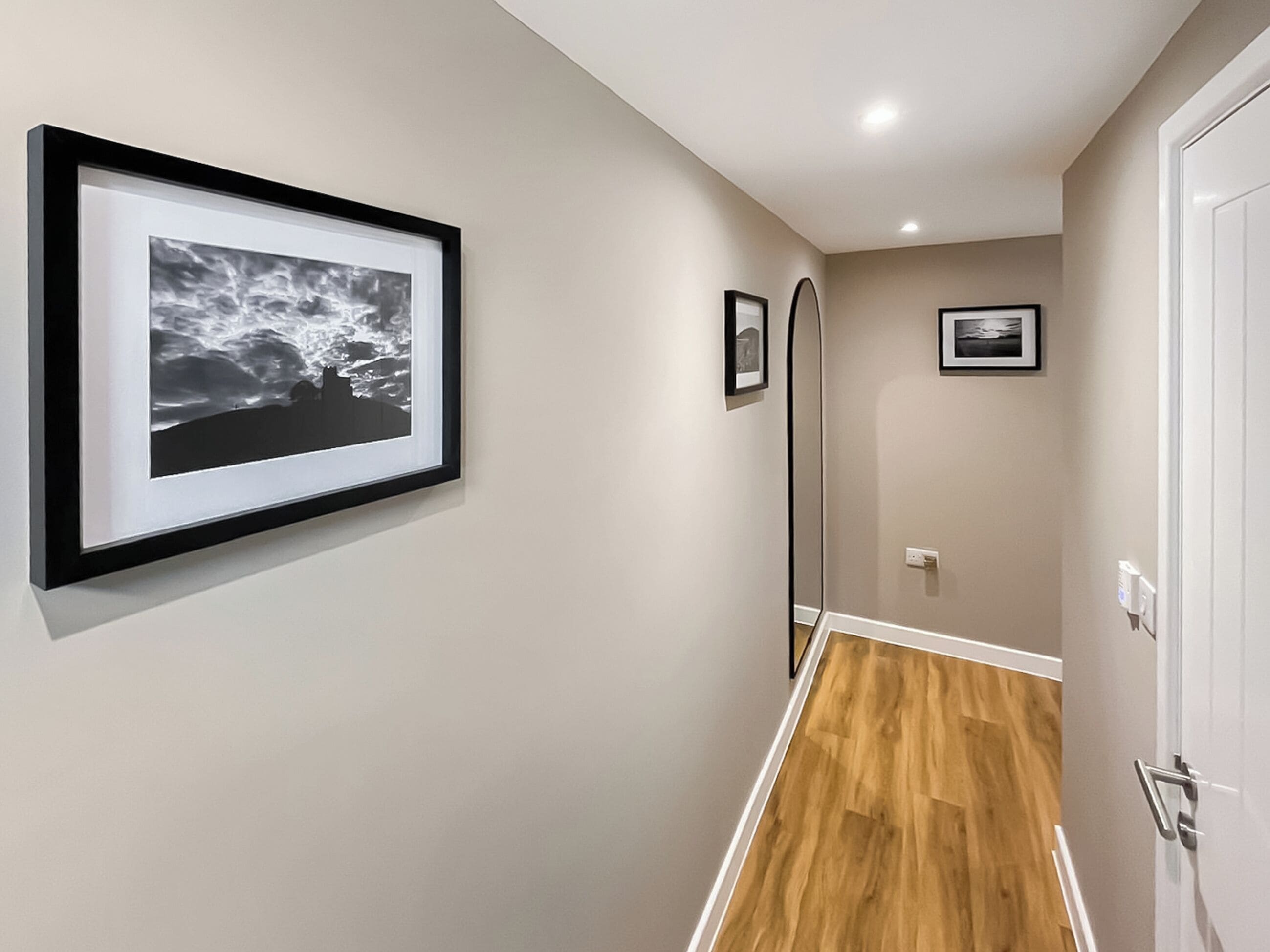 A hallway with framed artwork on the walls, a wooden floor, and a white door.