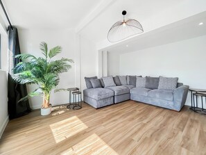 Ein modernes Wohnzimmer mit einem grauen Ecksofa, einer Topfpflanze und einer außergewöhnlichen Deckenleuchte.
