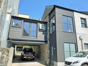 A modern two-story building with a garage entrance, a stone wall, and a parked truck. - 3 bedroom accommodation in Tavistock (Tavistock)