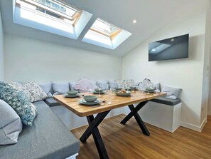 A modern dining area with a wooden table, grey cushions, and a flat-screen TV mounted on the wall. - 3 bedroom accommodation in Tavistock (Tavistock)