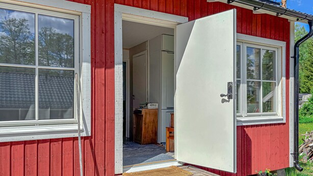 En röd träbyggnad med en vit dörr och vita fönster.