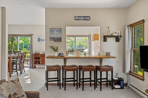 A cozy kitchen with a bar area, wooden stools, and a large window offering a view of greenery. - Group-Friendly Stay + Deck Dining + BBQ | Near Ski + Waterparks | Aspen Hollow (Tannersville)