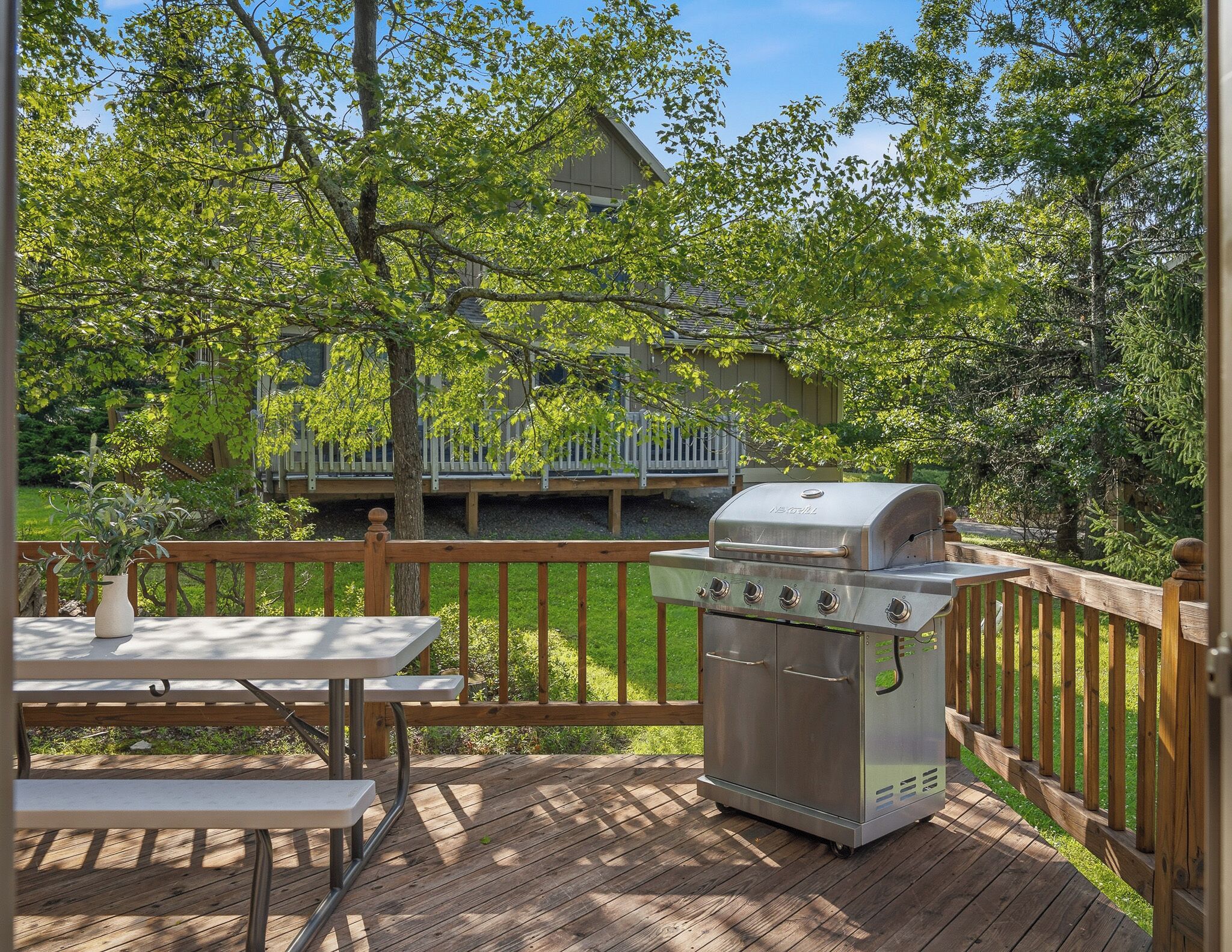 Une terrasse en bois avec un barbecue et une table, entourée d’une clôture en bois et d’arbres.