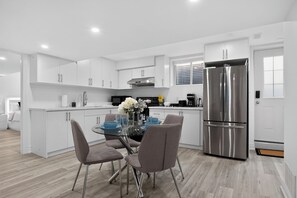 A modern kitchen with white cabinetry, a stainless steel refrigerator, and a dining area with a glass table and chairs. - Luxury 2BR Basement near Wonderland/Vaughan, Wi-Fi (Vaughan)