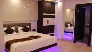 Une chambre moderne avec un grand lit, une armoire intégrée et une salle de bain visible à travers une porte ouverte.