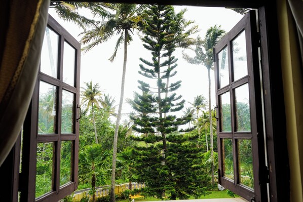 An open window with a view of a lush green landscape, including a tall coniferous tree and palm trees.