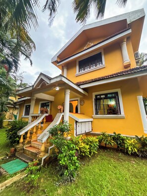 A two-story house with a porch, a staircase, and a small garden area. - Luxury 3BHK Sea View Villa – Velsao, South Goa (Velsao)
