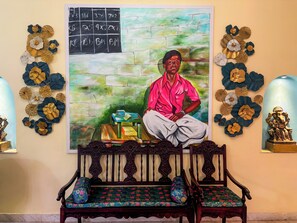 Une pièce dans laquelle on trouve un grand tableau représentant un homme, un banc en bois avec des coussins et des œuvres d’art décoratives accrochées au mur.