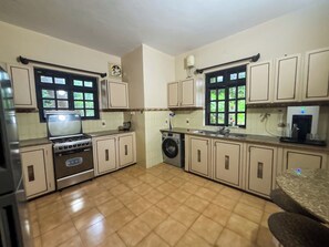 A kitchen with a stove, oven, washing machine, and a water dispenser. - Luxury 3BHK Sea View Villa – Velsao, South Goa (Velsao)