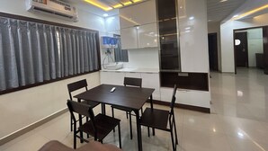 Uma área de refeições moderna com mesa, cadeiras, ventilador de teto e cozinha equipada com pia e armários.