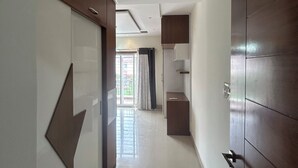 Um corredor com design moderno, apresentando uma grande decoração em formato de seta na parede esquerda, uma porta de madeira à direita e vista para um quarto com janela e cortinas.